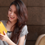 Young female travel nurse opening yellow present box and smiling excited at the gift.