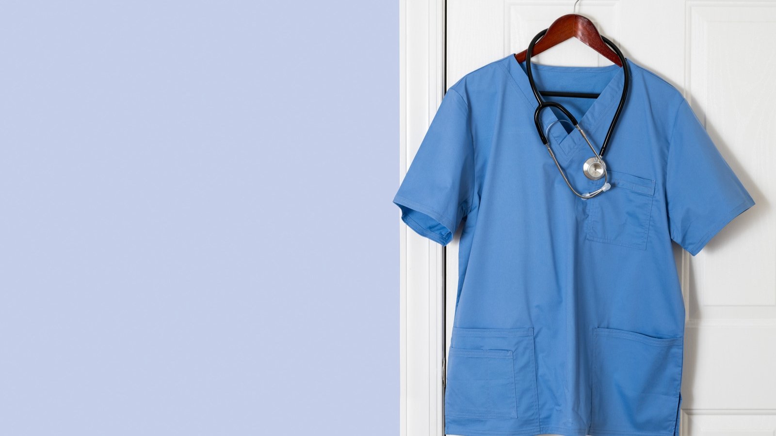 Blue scrubs hanging on white door on hanger against a light blue wall.