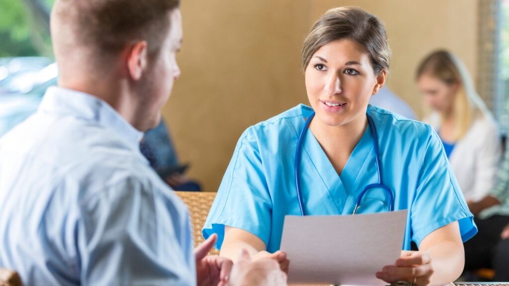 Travel nurse interviewing man in a blue dress shirt and asking top Travel Nursing Interview Questions