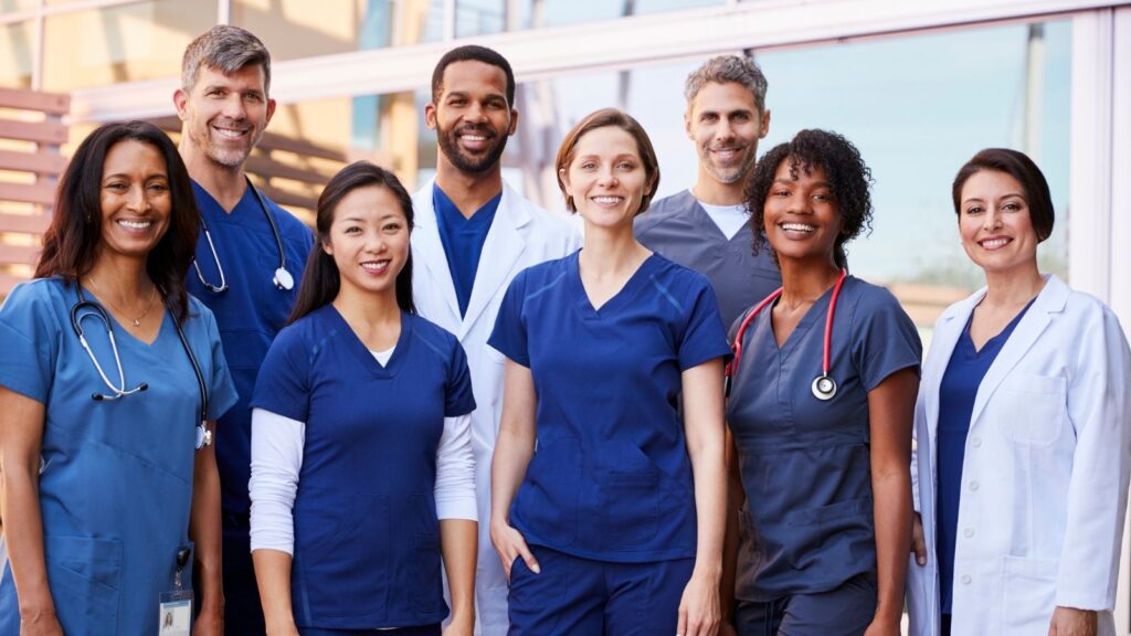 Group of multicultural diverse travel nurses happy and smiling in scrubs.