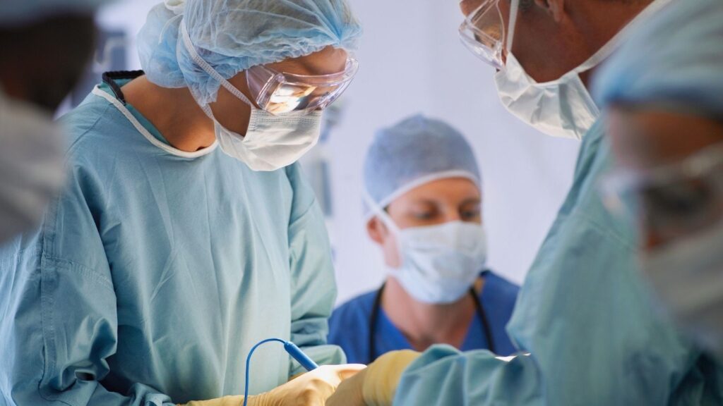 Travel allied health helping with a surgery operation while wearing scrubs.
