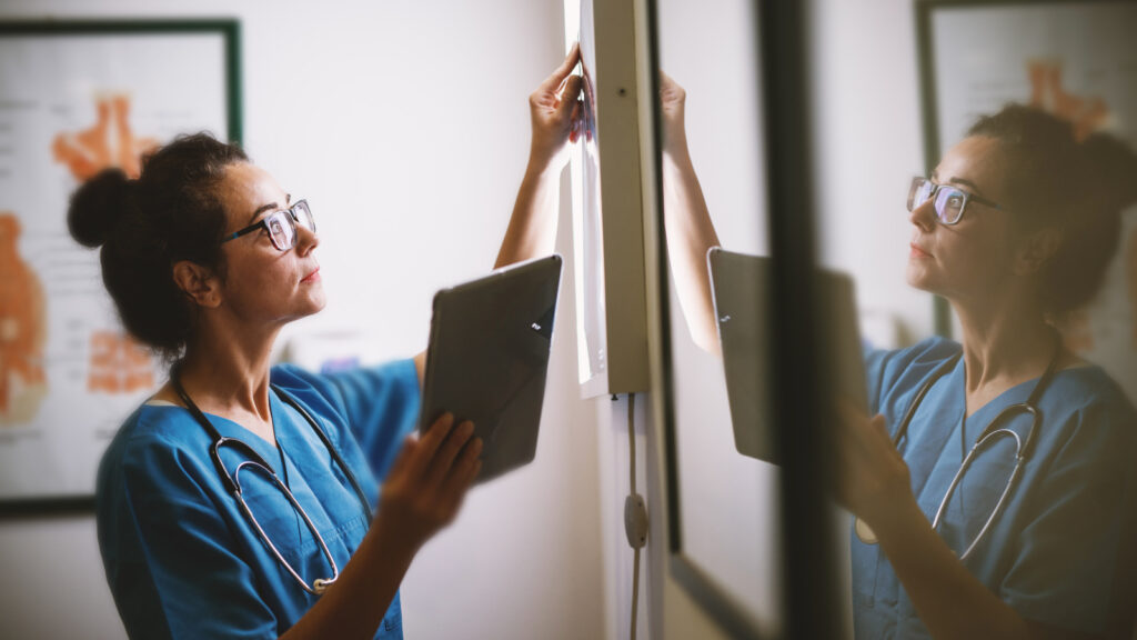 Female nurse with glasses examining x-rays on a light box.