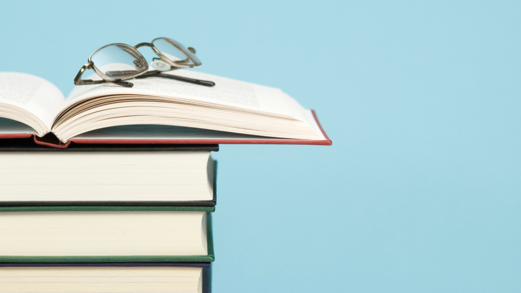 Pair of glasses placed on top of books with blue background.