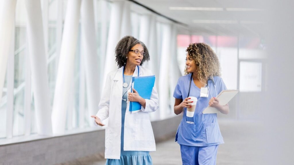 Two smiling female nurses walking down a hallway and talking at one of the best hospitals in Michigan for travel nurses