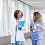 Two smiling female nurses walking down a hallway and talking at one of the best hospitals in Michigan for travel nurses