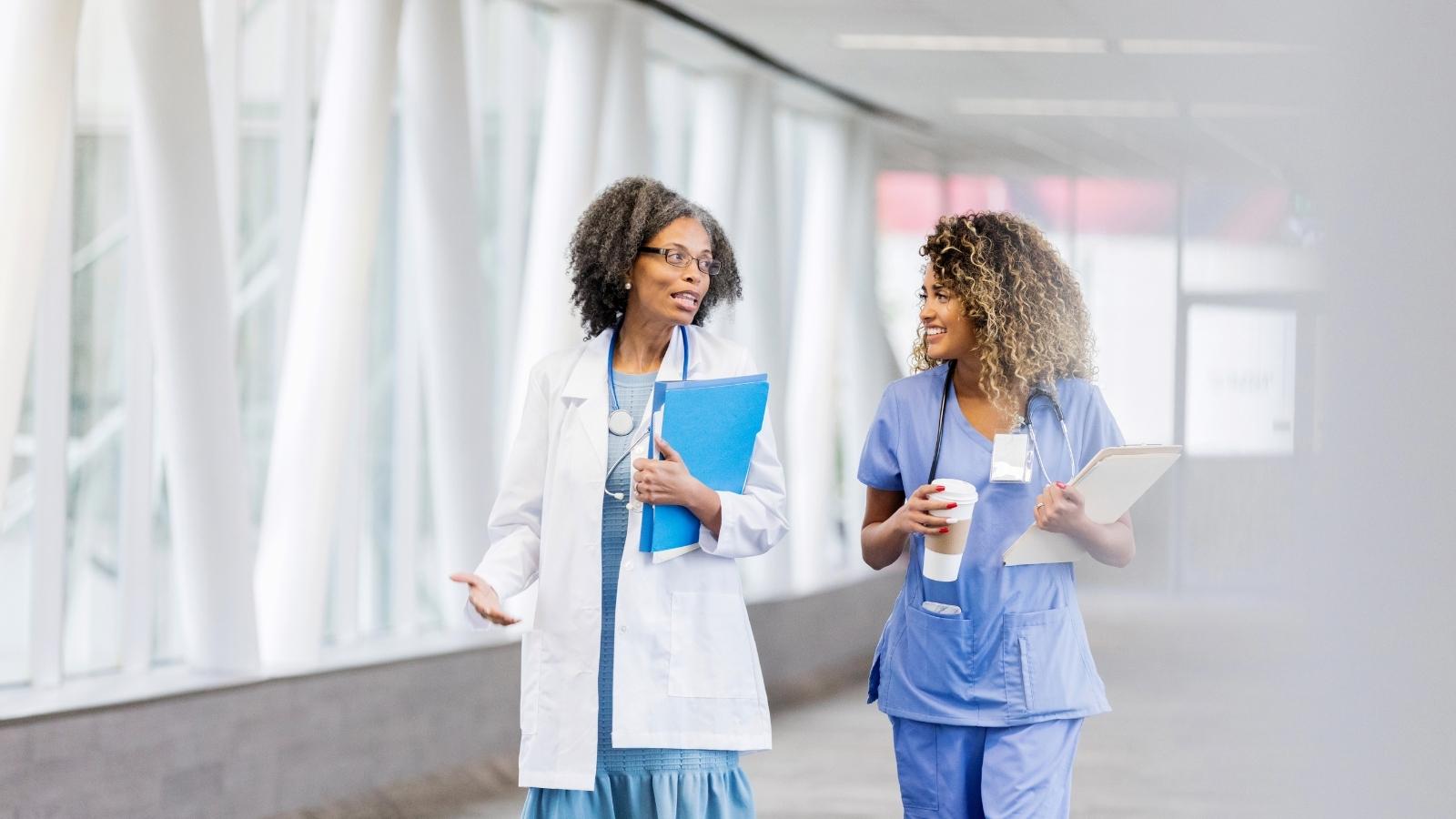Two smiling female nurses walking down a hallway and talking at one of the best hospitals in Michigan for travel nurses