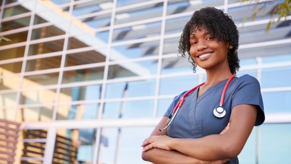 African American nurse standing in front of a building and smiling.