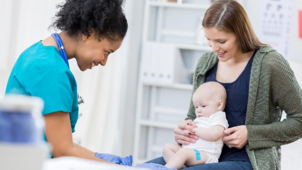 Female African American pediatric nurse smiling at a baby and mother.
