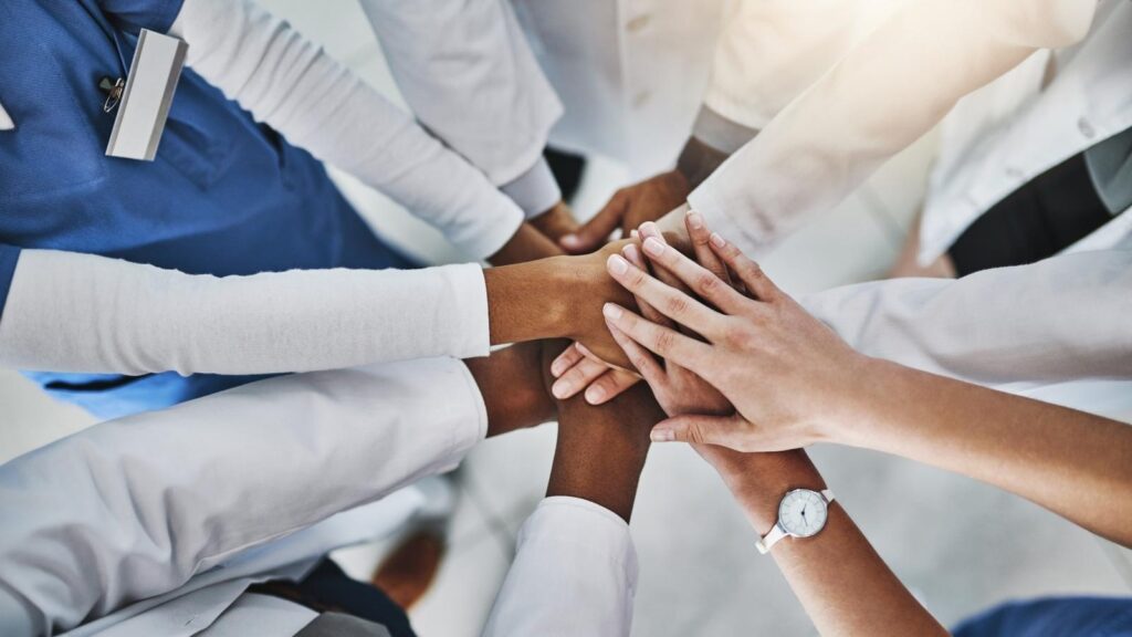 Diverse nurses and allied health with their hands joined in the middle.