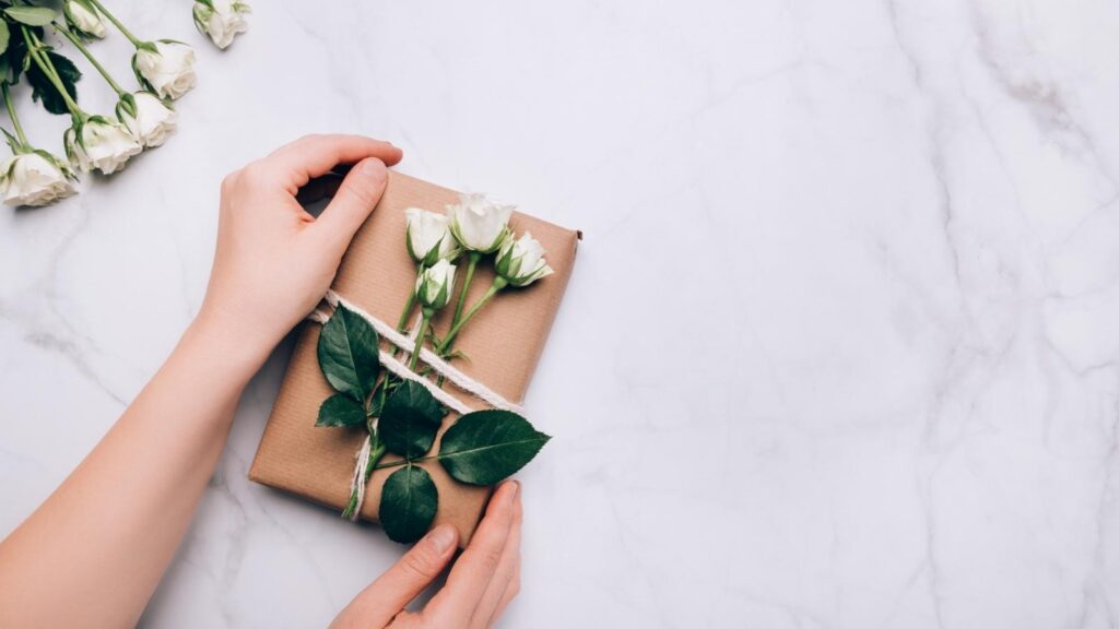 Hands arranging a gift with minimalistic eco-friendly packaging on a marbled table.