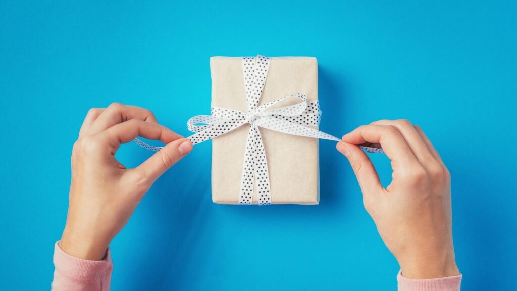 Hands opening a small nurse gift on a blue table.