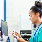 Travel nurse looking at a clipboard and sitting in an office at a table in post-acute-care