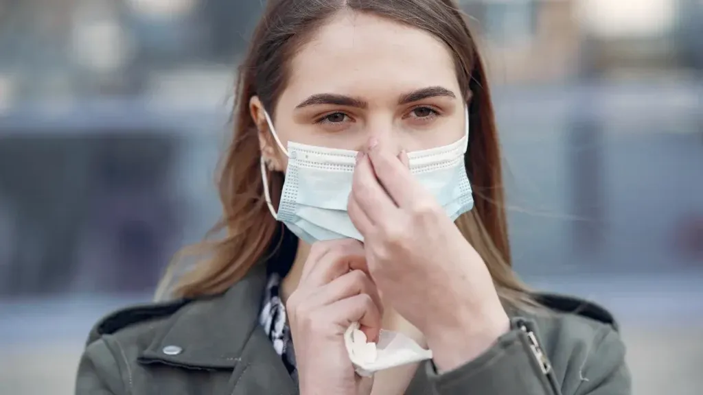 Young woman outdoors adjusting her mask while holding a white tissue after blowing her nose from the flu.
